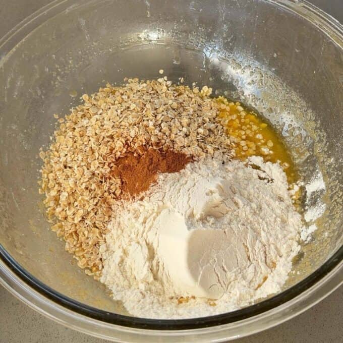 Feijoa and Pear Crumble A glass bowl containing oats, melted butter, flour, and ground cinnamon, ready to be mixed on a kitchen countertop.