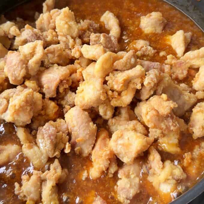 Sticky Orange Chicken Thighs Close-up of fried chicken pieces in a pan with orange-colored sauce or gravy.