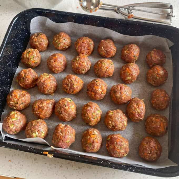 Veggie-Packed Meatballs A baking tray lined with parchment paper holds five rows of uncooked meatballs, evenly spaced and ready to be cooked.