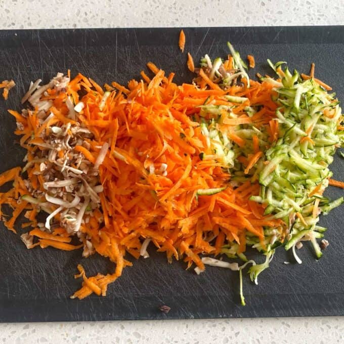 Veggie-Packed Meatballs Grated carrots, zucchini, and chopped mushrooms arranged in separate piles on a black cutting board.