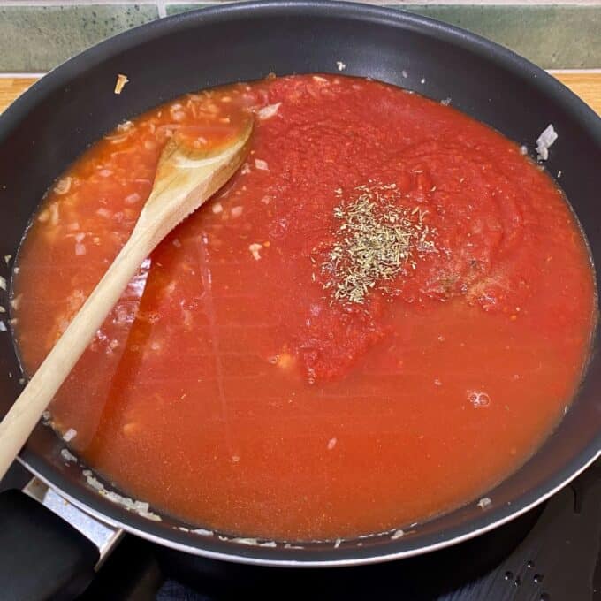 Veggie-Packed Meatballs A frying pan with tomato sauce, chopped onions, and dried herbs being stirred with a wooden spoon on a stovetop.