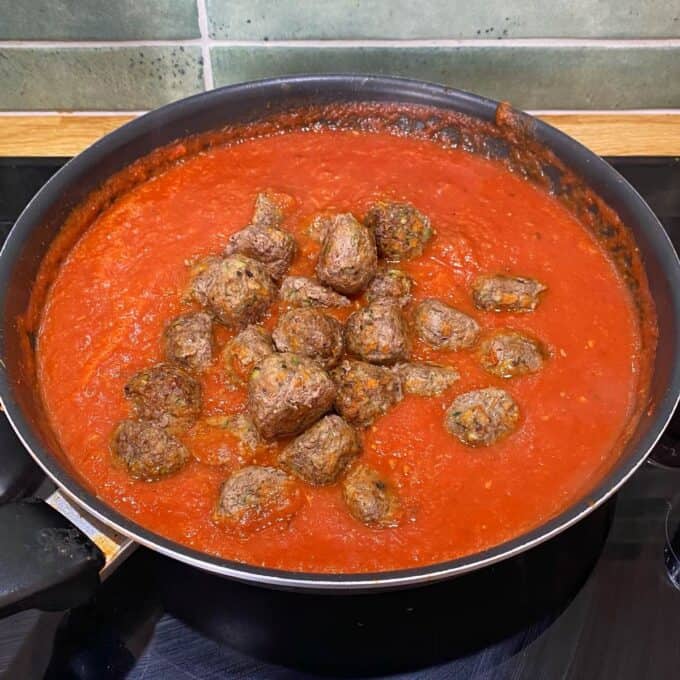 Veggie-Packed Meatballs A frying pan filled with tomato sauce and meatballs sits on a stovetop, with green tiles and a wooden trim visible in the background.