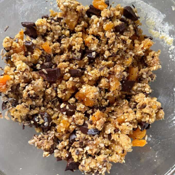 Apricot Bumper Bars A close-up of a bowl containing an unbaked mixture of oats, chopped dried apricots, and chunks of dark chocolate.