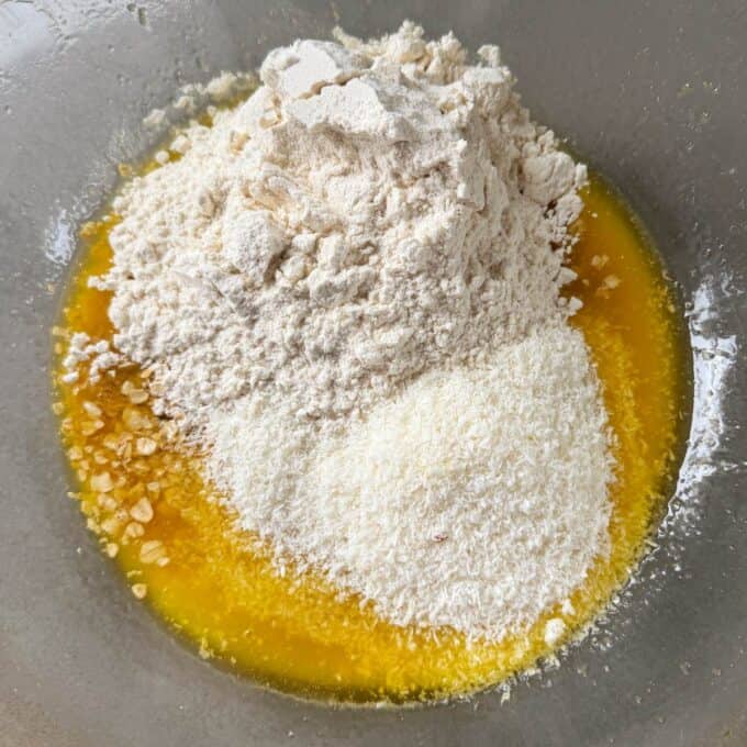 Apricot Bumper Bars A glass bowl containing melted butter, shredded coconut, flour, and chopped nuts, ready to be mixed for baking.