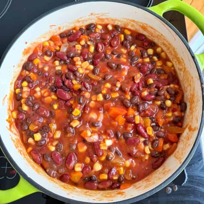 Baked Vegetarian Chilli A pot of chili with kidney beans, black beans, corn, diced tomatoes, and chopped carrots, simmering on a stovetop.