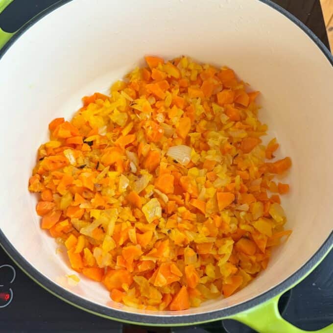 Baked Vegetarian Chilli Chopped carrots, onions, and yellow bell peppers sautéing in a large white pot on a stovetop.