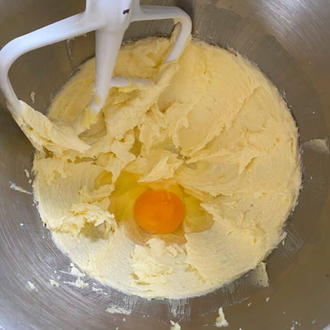 Bakewell Tart A mixing bowl with creamed butter and sugar, and a raw egg cracked in the center, next to a white paddle attachment.