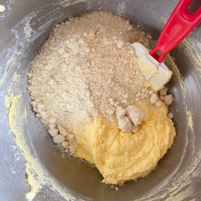 Bakewell Tart A mixing bowl with creamed butter and sugar, almond flour, and a red spatula, showing ingredients being combined for baking.