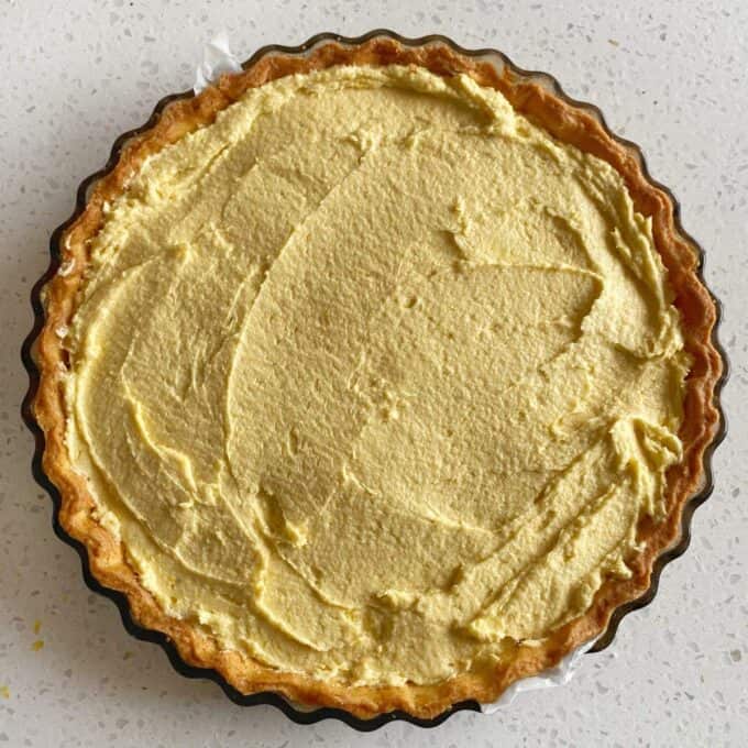 Bakewell Tart Unbaked tart with a smooth, creamy yellow filling in a round, fluted tart pan on a speckled countertop.