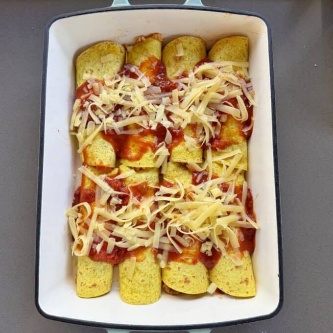 Cheesy Chicken Enchiladas A baking dish filled with rolled tortillas topped with red sauce and shredded cheese, ready to be baked.