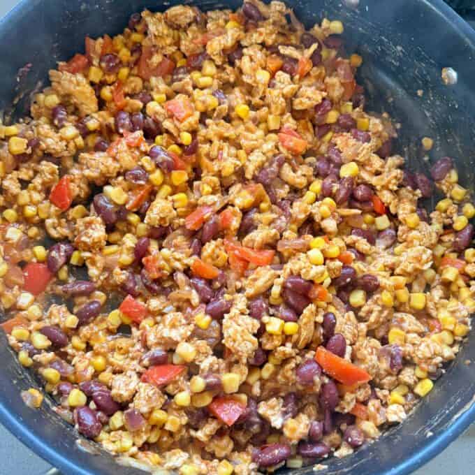 Cheesy Chicken Enchiladas A large pot filled with a cooked mixture of ground meat, kidney beans, corn, and diced red peppers.