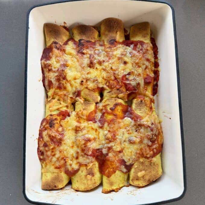 Cheesy Chicken Enchiladas A rectangular baking dish filled with eight baked enchiladas topped with melted cheese and tomato sauce.