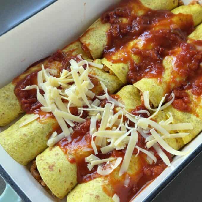 Cheesy Chicken Enchiladas A baking dish containing rolled tortillas filled with ingredients, topped with tomato sauce and shredded cheese, ready to be baked.