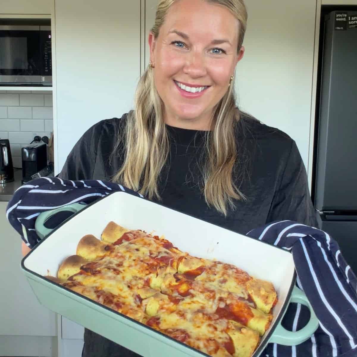 Cheesy Chicken Enchiladas A woman holds a baking dish filled with baked enchiladas topped with melted cheese, smiling in a modern kitchen.