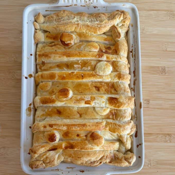 Chicken and Leek Pie Golden-brown rectangular puff pastry pie in a white baking dish, with decorative pastry strips and circles on top, on a wooden surface.