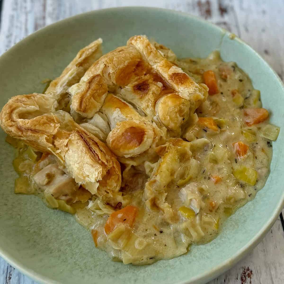Chicken and Leek Pie A serving of creamy chicken and vegetable pot pie filling topped with flaky puff pastry in a light green bowl.