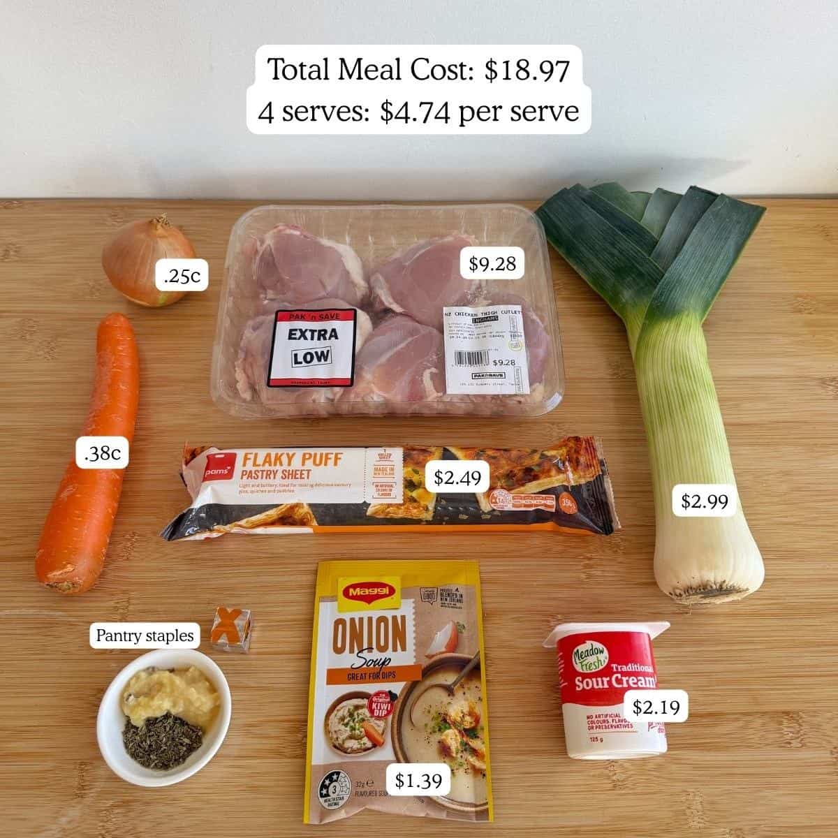 Chicken and Leek Pie Ingredients for a meal are arranged on a wooden surface with labeled prices, including chicken, leek, carrot, puff pastry, soup mix, sour cream, and pantry staples.