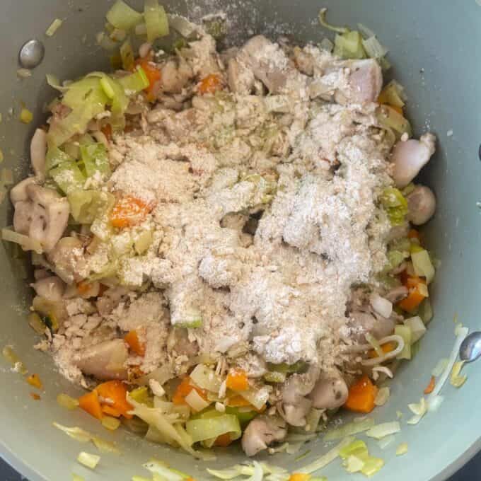 Chicken and Leek Pie Chopped vegetables and pieces of chicken are being cooked in a pot, topped with a layer of flour.
