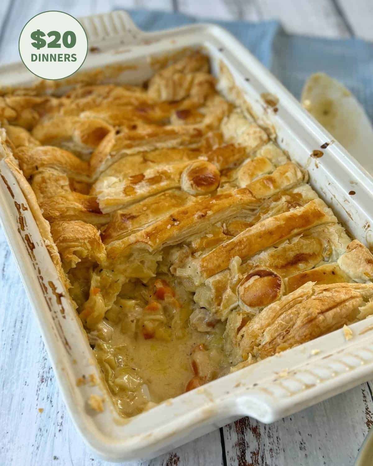 Chicken and Leek Pie Rectangular casserole dish with a golden, flaky puff pastry topping over a creamy vegetable filling; a portion has been served. A sticker reads $20 Dinners.