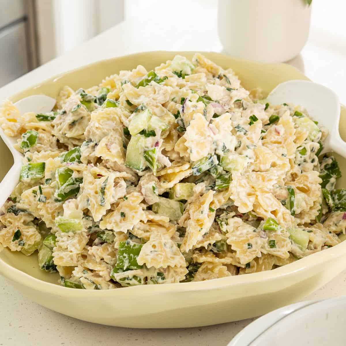 Herby Chicken Pasta Salad A bowl of pasta salad with bowtie pasta, chopped celery, green onion, and a creamy dressing, served with white salad utensils.