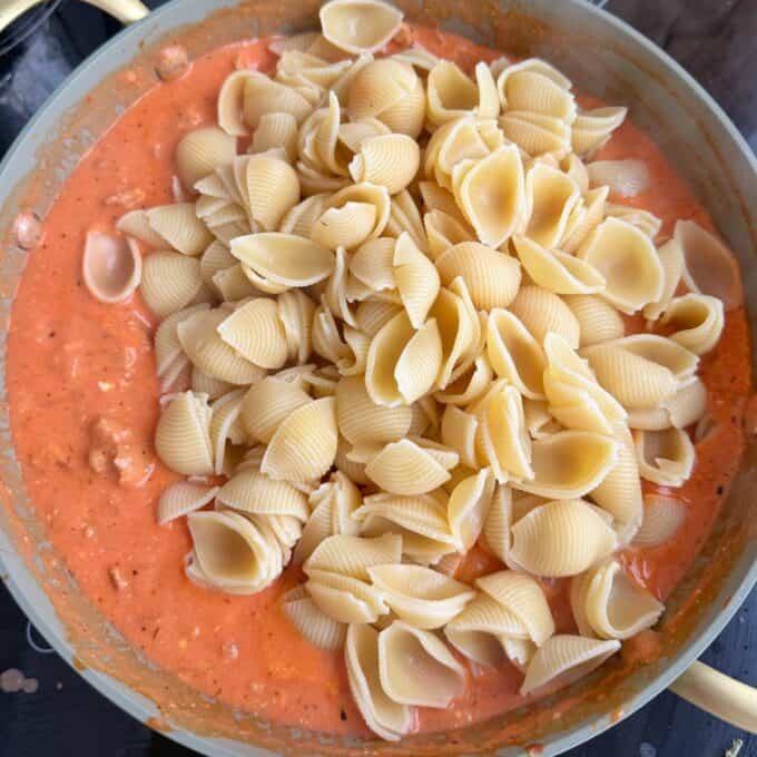 Italian Sausage Pasta Bake Uncooked pasta shells sitting on top of creamy tomato sauce in a large skillet on a stovetop.
