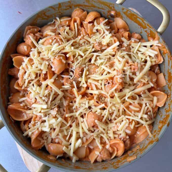 Italian Sausage Pasta Bake A pan of cooked pasta shells in tomato sauce topped with shredded cheese, ready to be mixed or baked.