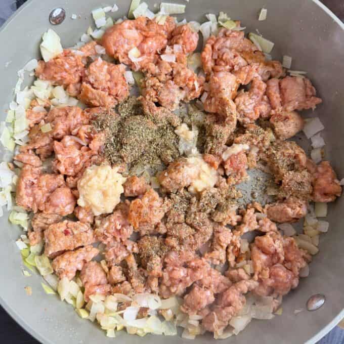 Italian Sausage Pasta Bake Ground meat, chopped onions, minced garlic, and dried herbs cooking in a large sauté pan.