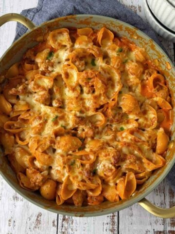 A pan of baked pasta shells with tomato sauce, ground meat, and melted cheese on top, placed on a wooden surface.