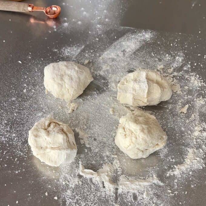 Lamb Koftas on Homemade Flatbreads Four pieces of raw dough rest on a floured surface, with a measuring spoon visible in the corner.