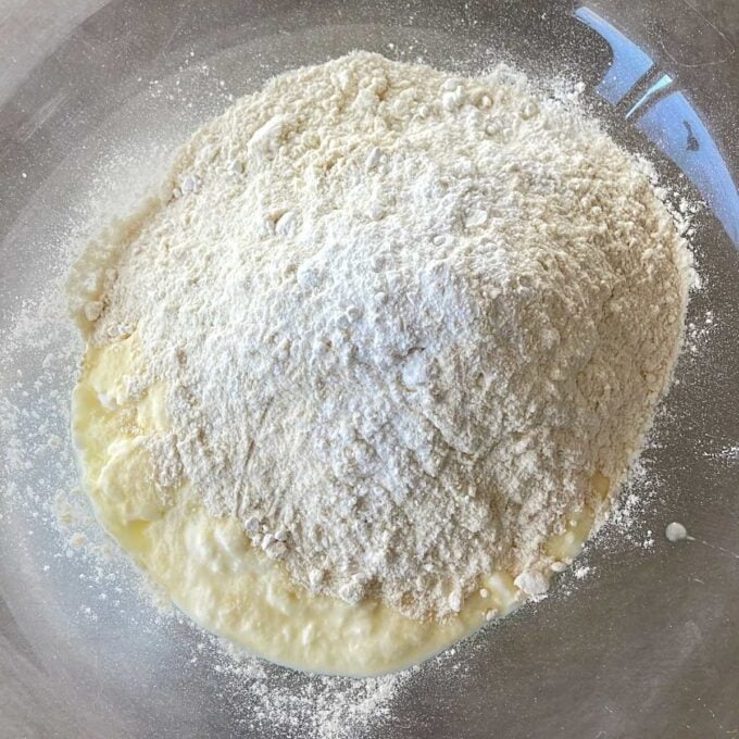 Lamb Koftas on Homemade Flatbreads A mound of flour sits on top of a pool of thick liquid, likely batter or dough ingredients, in a clear mixing bowl.