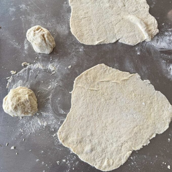 Lamb Koftas on Homemade Flatbreads Two flattened pieces of dough and two dough balls on a floured surface, prepared for baking or cooking.