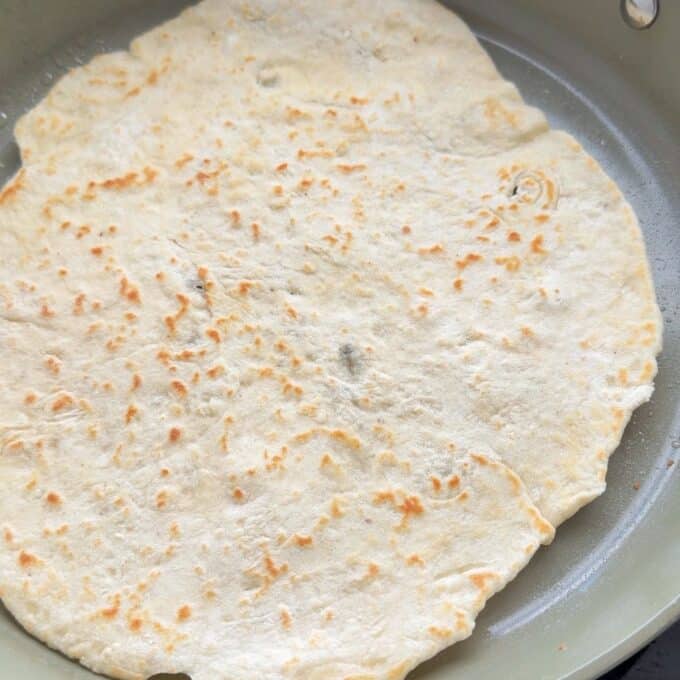Lamb Koftas on Homemade Flatbreads A flat, round piece of dough is cooking in a skillet, showing light browning and some flour on its surface.