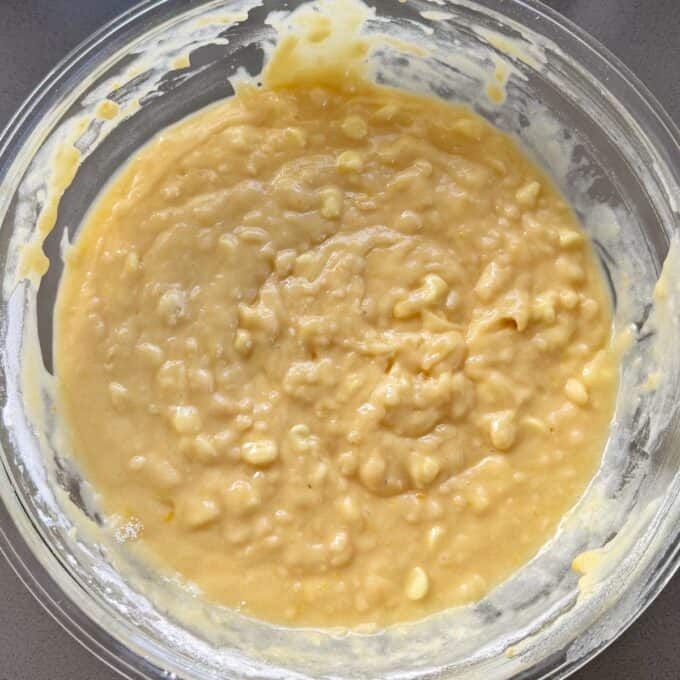 Lemon, Yoghurt and White Chocolate Muffins A glass bowl filled with thick, yellow batter containing visible lumps and small pieces, likely for baking or cooking preparation.