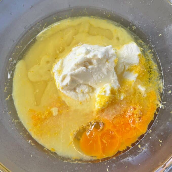 Lemon, Yoghurt and White Chocolate Muffins A glass bowl containing cracked eggs, melted butter, and a dollop of sour cream, ready to be mixed.