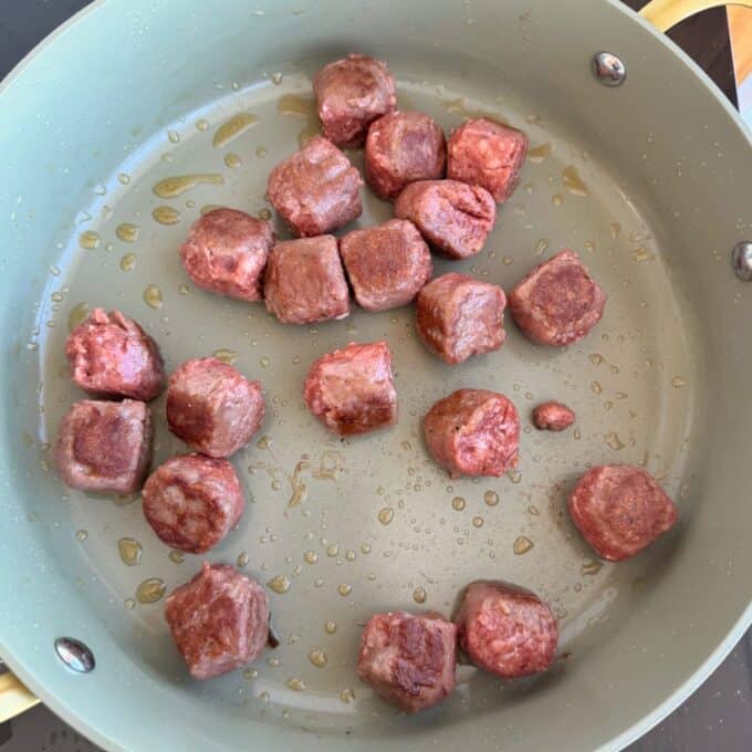 Meatball Noodle Stir Fry Raw beef cubes are sizzling in a lightly oiled frying pan, beginning to brown on some sides.