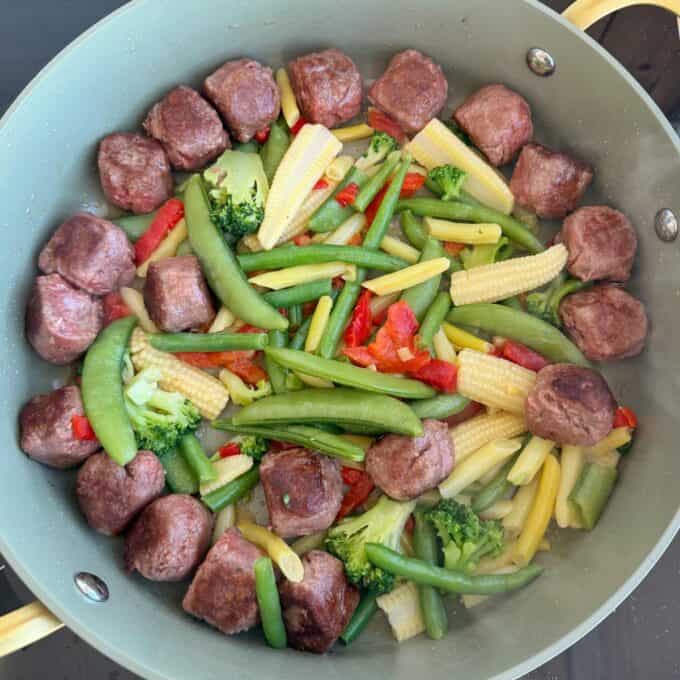 Meatball Noodle Stir Fry A pan filled with meatballs, snap peas, baby corn, broccoli, red bell pepper, and yellow beans arranged in a circular pattern.
