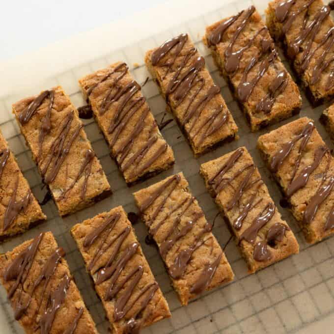 Oaty Choc Chunk Cookie Bars Rectangular cookie bars arranged on a wire rack topped with a drizzle of chocolate, set on a sheet of parchment paper.