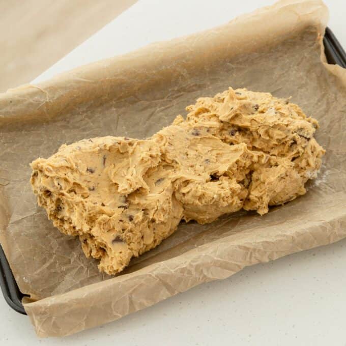 Oaty Choc Chunk Cookie Bars A mound of chocolate chip cookie dough sits on a baking tray lined with parchment paper.