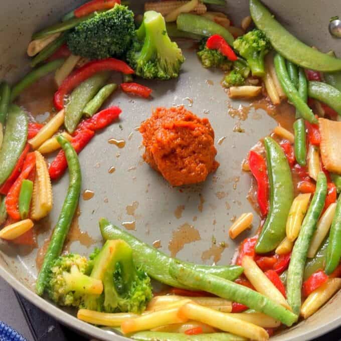 One Pot Beef Curry with Noodles A pile of orange paste is in the center of a pan with stir-fried vegetables including broccoli, snap peas, red bell peppers, and baby corn.