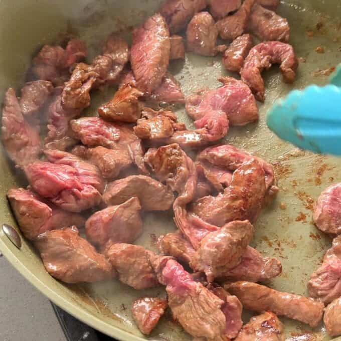 One Pot Beef Curry with Noodles Bite-sized pieces of raw steak are being cooked in a light-colored pan.
