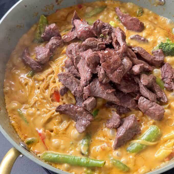 One Pot Beef Curry with Noodles A skillet of beef stir-fry with noodles, broccoli, snap peas, and a creamy orange sauce.