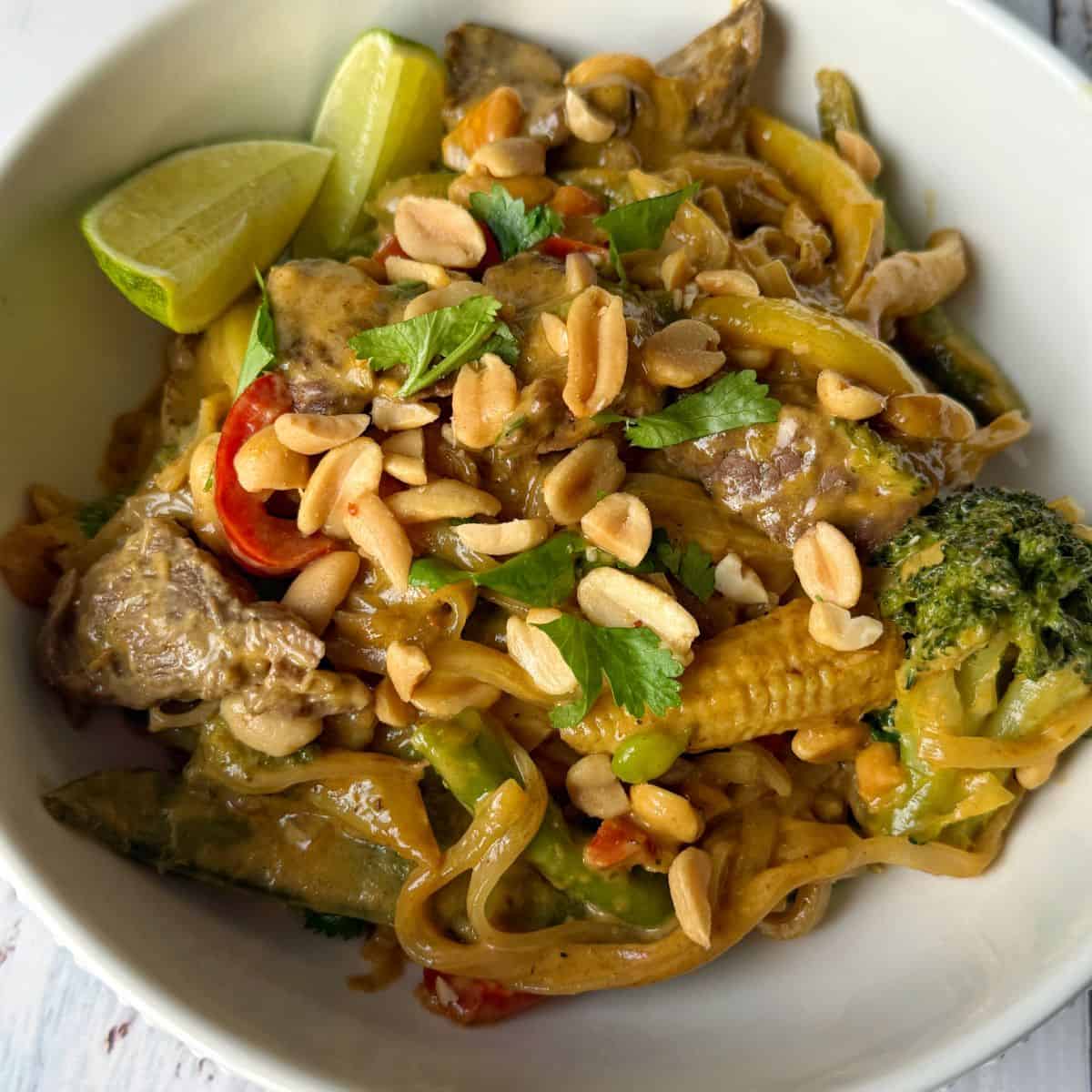 One Pot Beef Curry with Noodles A bowl of noodles with vegetables, peanuts, and lime wedges.