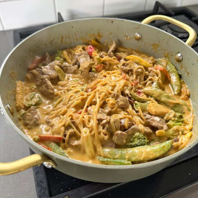 One Pot Beef Curry with Noodles A pan of noodles with sliced meat and vegetables in a creamy sauce.
