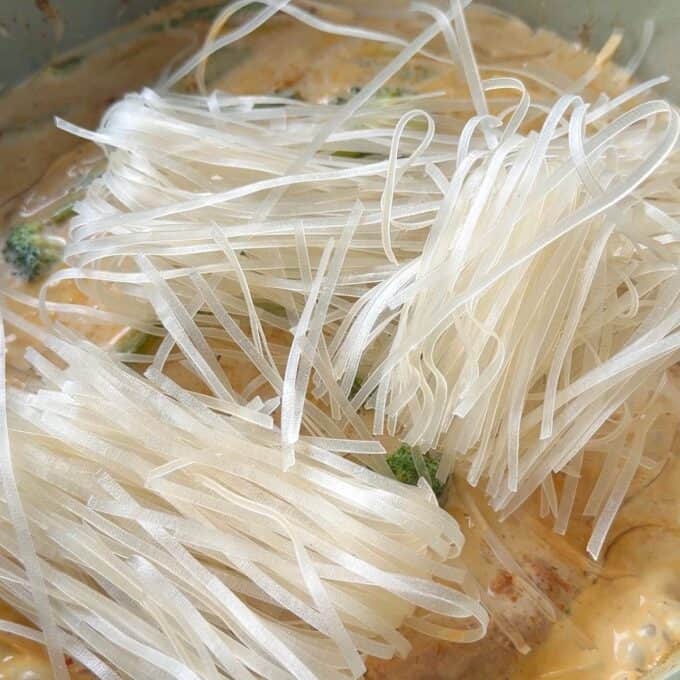 One Pot Beef Curry with Noodles Close-up of uncooked rice noodles placed over a creamy curry with broccoli.