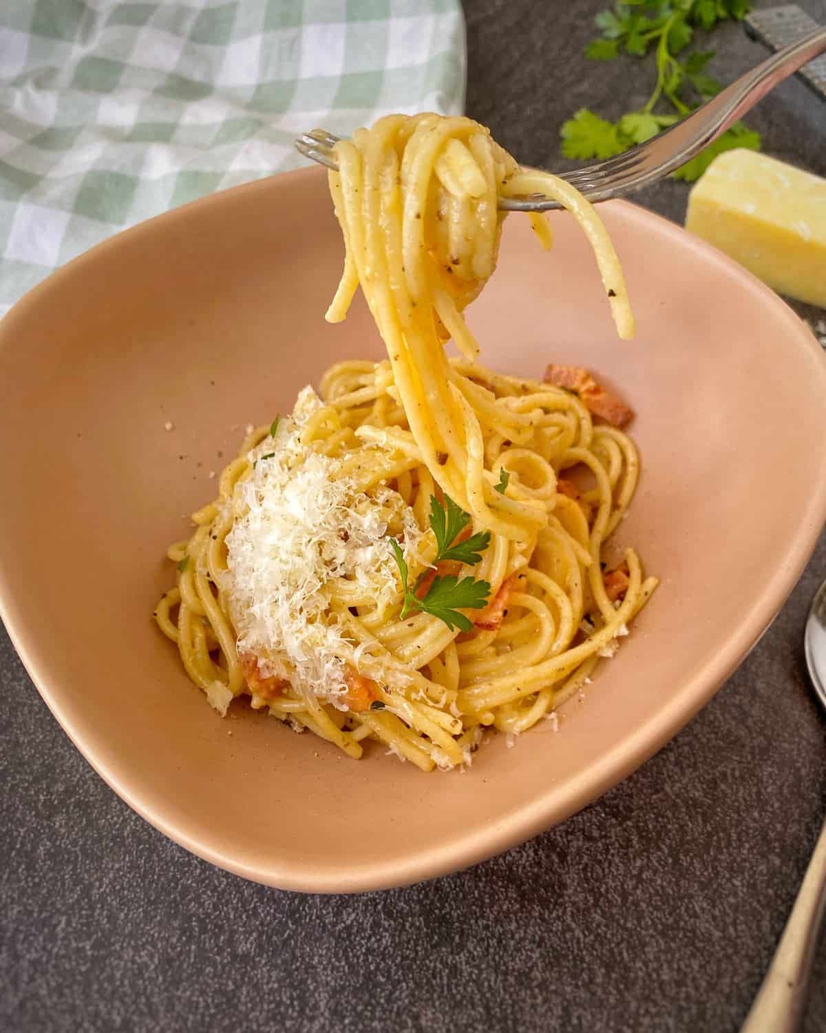 Spaghetti Carbonara A bowl of spaghetti topped with grated cheese and parsley; a fork lifts a portion of the pasta. A napkin, cheese, and herbs are in the background.
