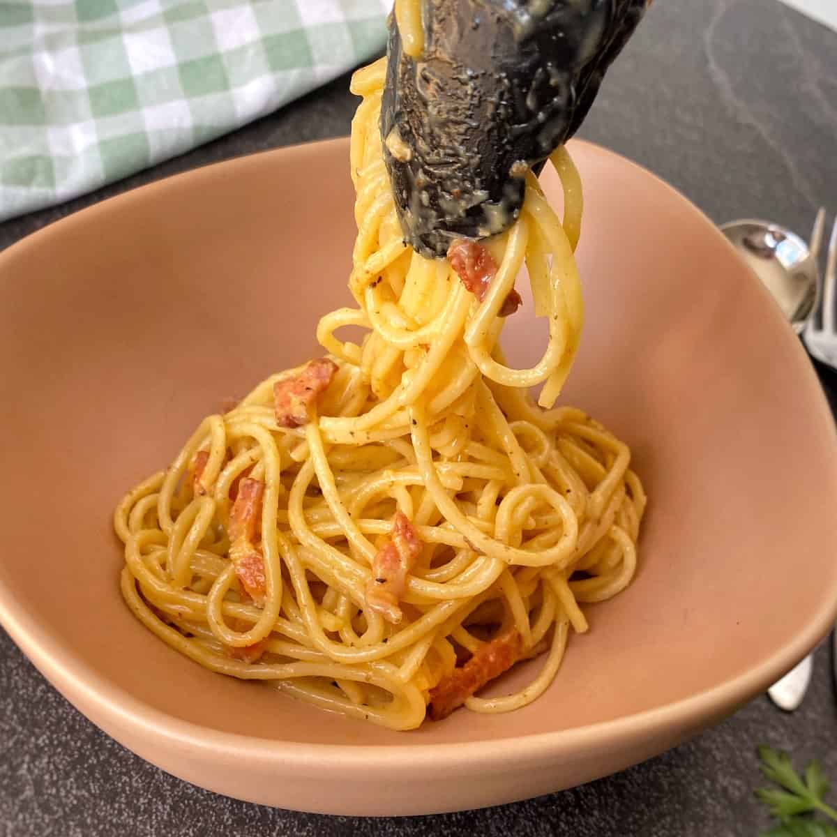 Spaghetti Carbonara A serving of spaghetti with a creamy sauce and pieces of bacon is being lifted with tongs from a bowl.
