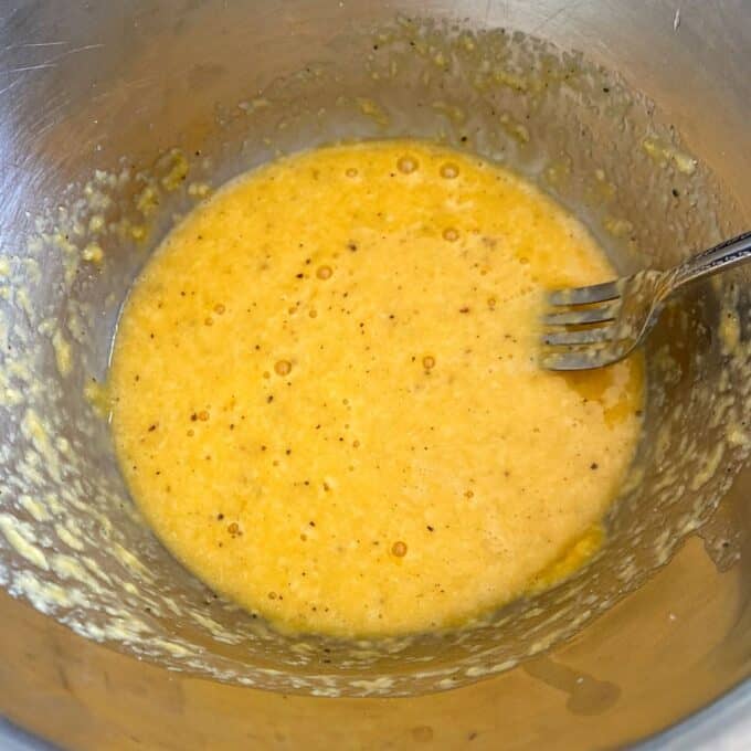 Spaghetti Carbonara A metal mixing bowl with a yellow, speckled liquid mixture and a metal fork resting inside.