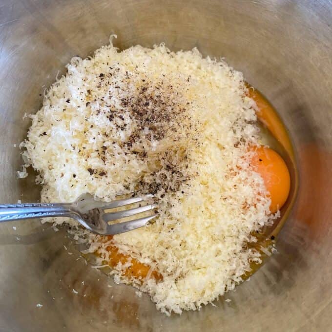 Spaghetti Carbonara A metal bowl containing grated cheese, two raw eggs, ground black pepper, and a fork.
