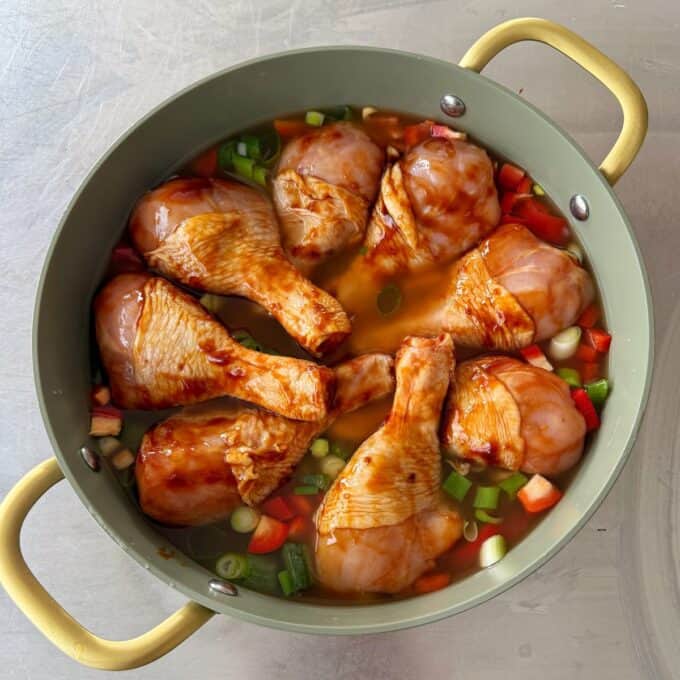 Teriyaki Chicken Drumsticks Raw marinated chicken drumsticks placed in a round pot with chopped green onions and red bell peppers, ready to be cooked.