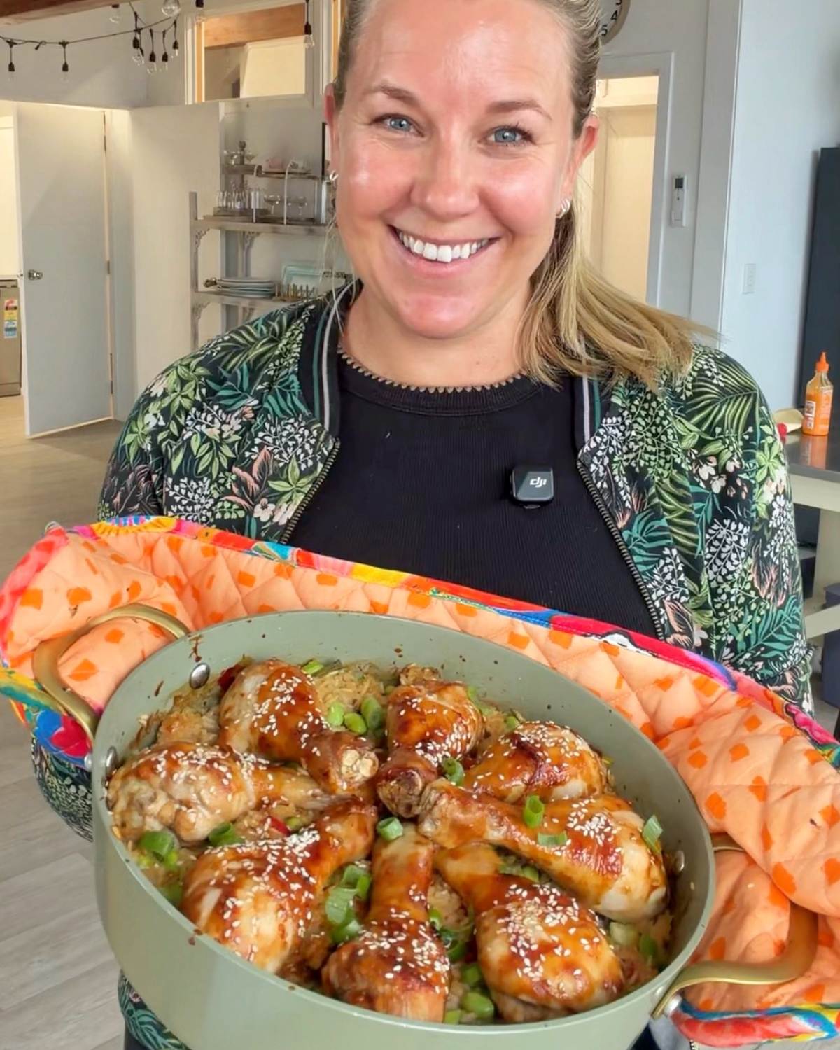 Teriyaki Chicken Drumsticks A woman smiles while holding a large pot filled with glazed chicken drumsticks topped with sesame seeds and chopped green onions.